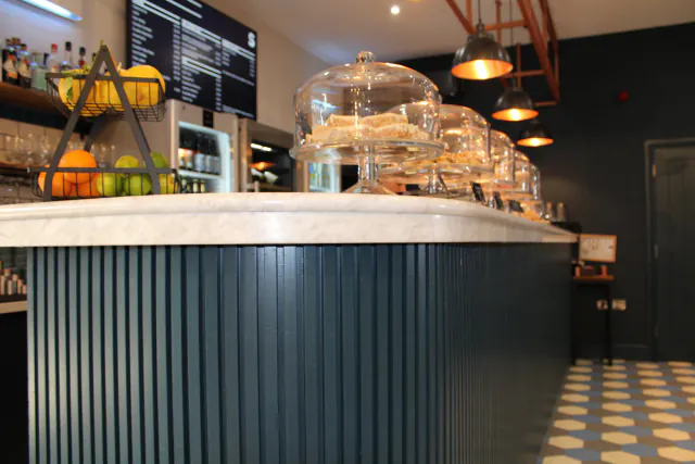 Barra de mármol de una cafetería de barrio con tartas bajo campanas de cristal